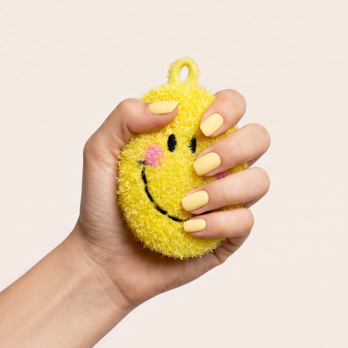 A hand squeezing the smiley face frubbies scrubber
