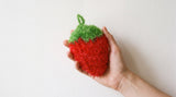 The strawberry scrubber resting in an open palm, showing it is about the size of a hand